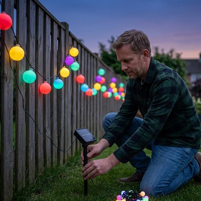 Guirlande lumineuse boule accrochee par homme sur cloture 